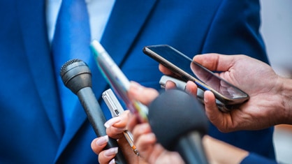 Man in a suit with a bunch of reporters